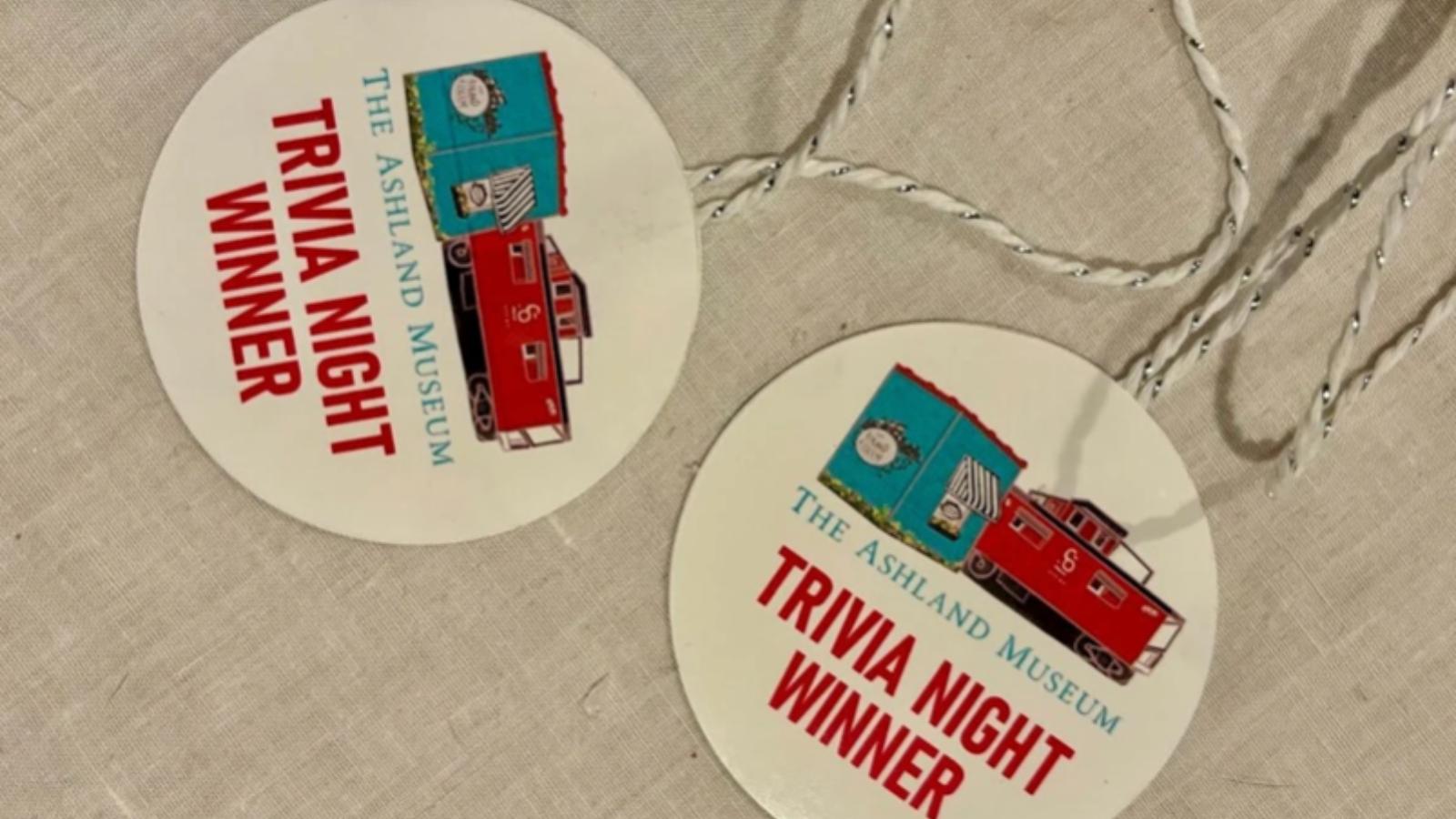 Two round badges say 'Trivia Night Winner' for The Ashland Museum, featuring a red locomotive and blue train cars on a light background.