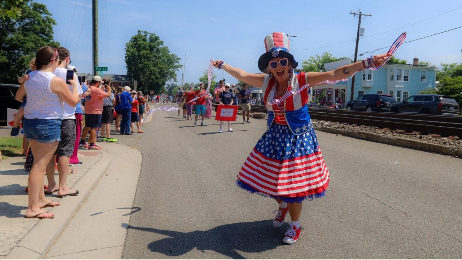 Ashland’s July 4th Parade & Celebration Woman in a red, white, and blue patriotic costume dances with arms outstretched during a parade on a sunny street lined with spectators.