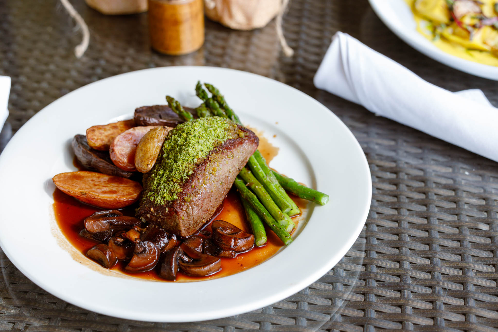 Beef tenderloin with herb crust, roasted potatoes, and asparagus in red sauce on a white plate.