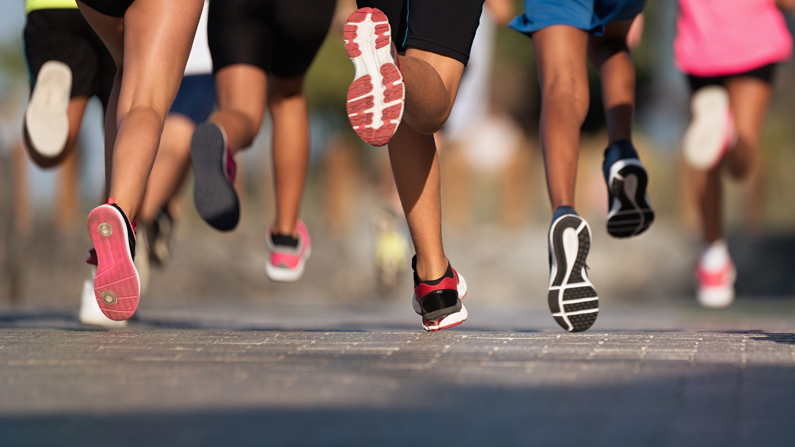 Runners sprinting on a road from behind, colorful athletic shoes in mid-stride.