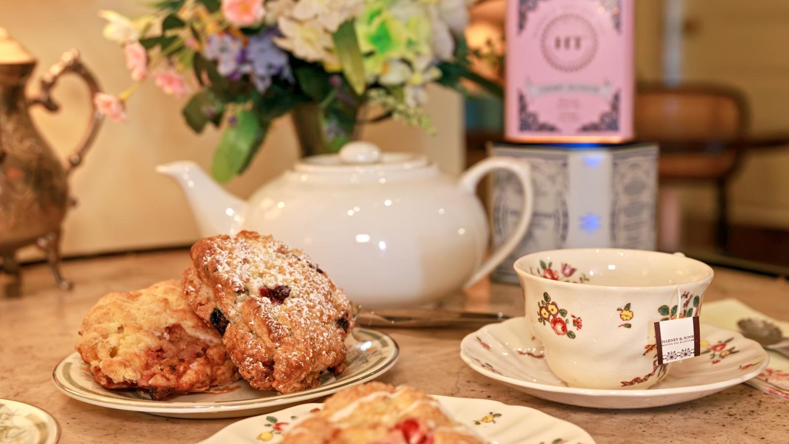 christmas in july-calendar header Plate with powdered-sugar muffins on a kitchen counter beside a white teapot and a floral teacup.